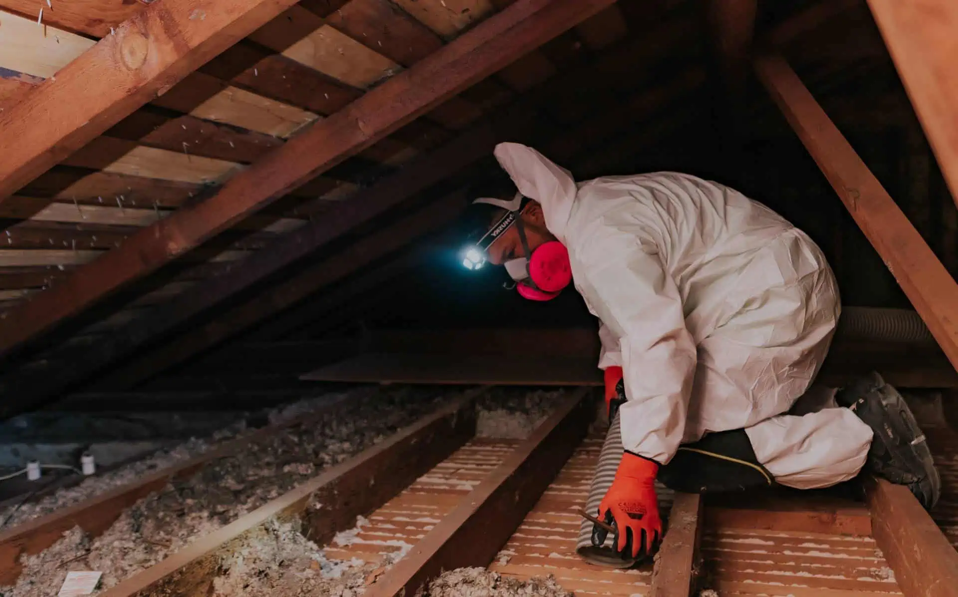 Attic Pros expert cleaning attic in white uniform and orange gloves