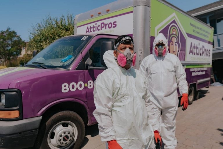 Attic Pros professionals in white uniform cleaning suits in front of work truck