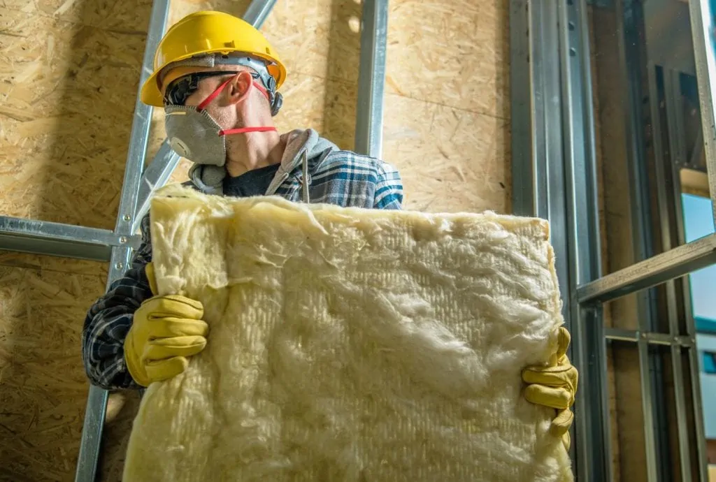 Attic Pros professional with yellow gloves and yellow hat carrying insulation