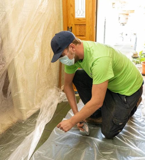 Attic Pros professional with green shirt putting down protective plastic in home