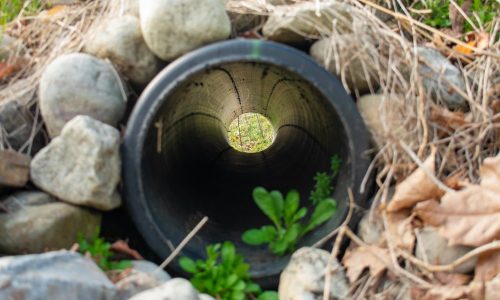 Looking Through a French Drain With a Black Pipe and Large Rocks Surrounding It